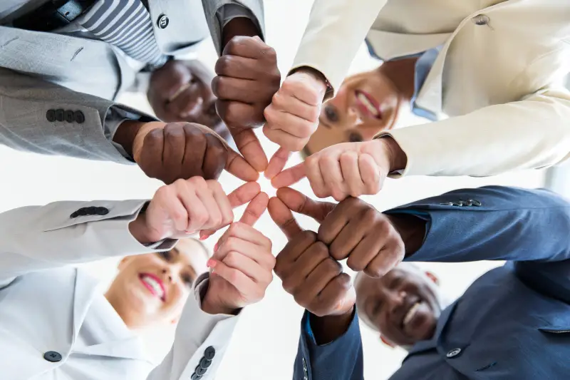 Stronger Communities low angle view of multiracial co-workers with thumbs joined together